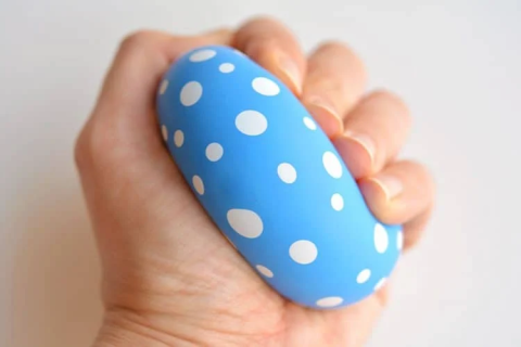 a hand squeezing a stress ball made from a blue and white polka dot balloon