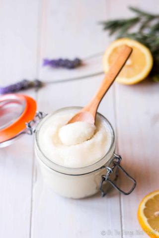 A close up of a small tub containing a sugar scrub and a small wooden spoon