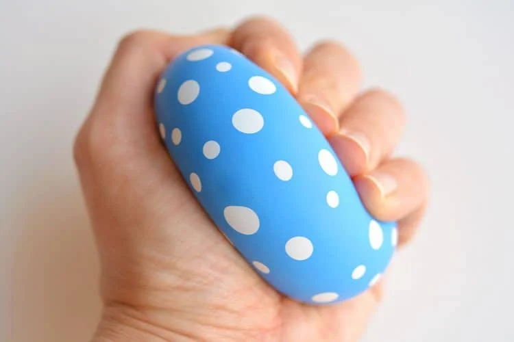 a hand squeezing a stress ball made from a blue and white polka dot balloon